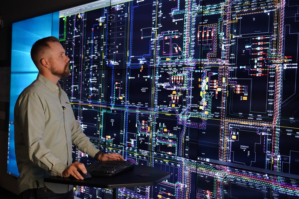 An APS Employee stands in front of a lighted signal board monitoring the grid