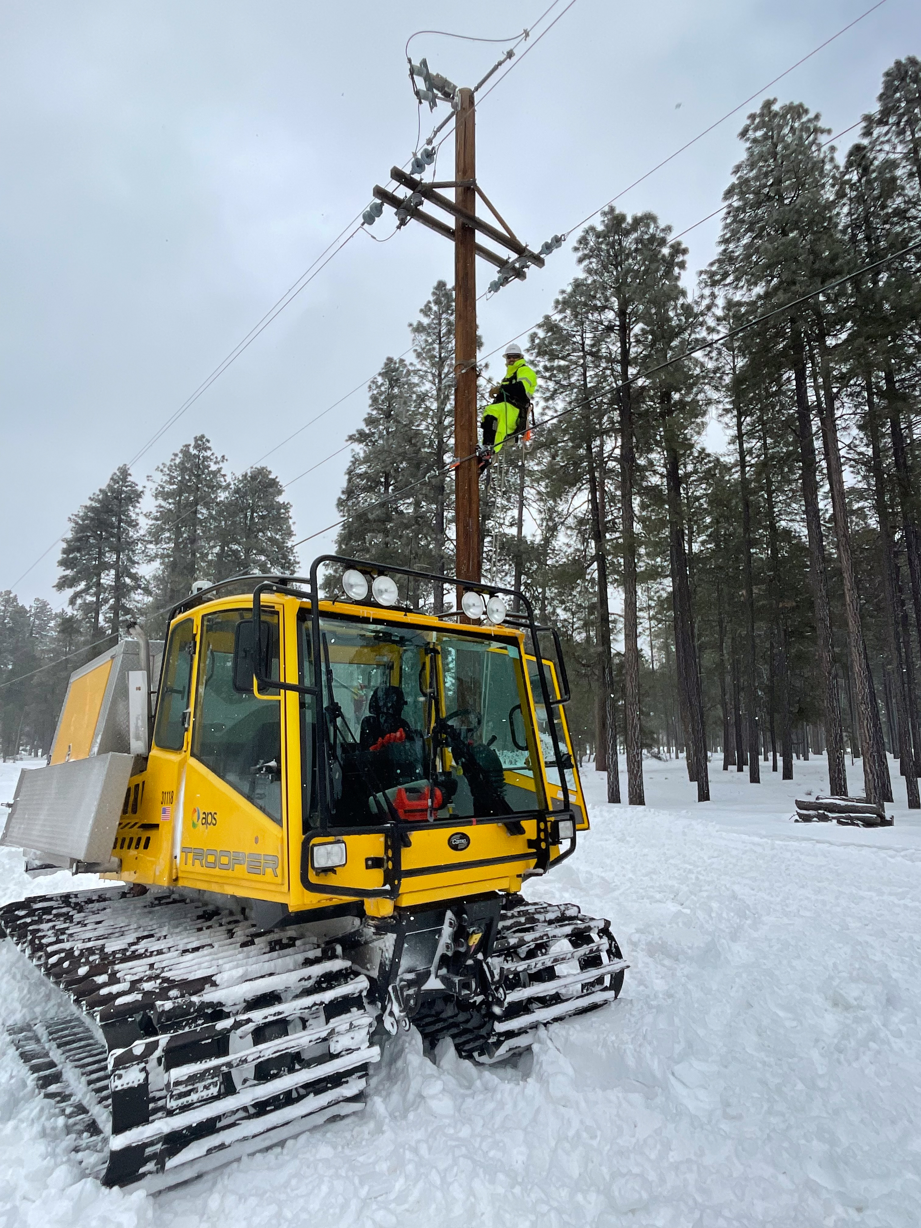 APS Lineman on a pole during a winter storm with a snowcat in the foreground