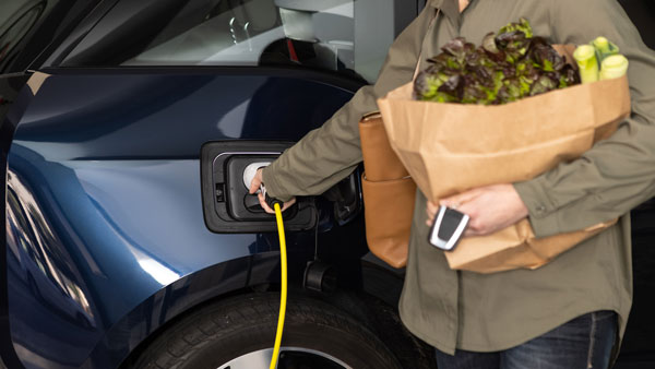 Woman carrying groceries plugging her car into a charger