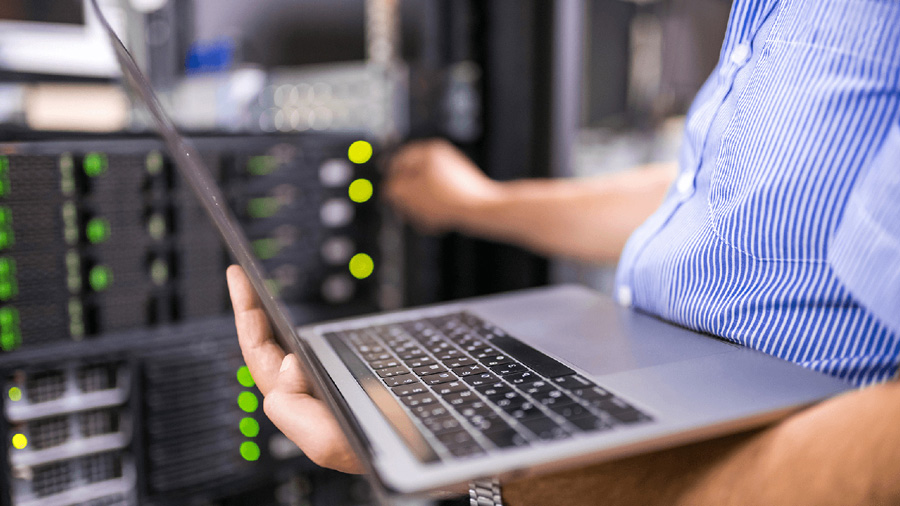Man holding a laptop and adjusting a control panel.
