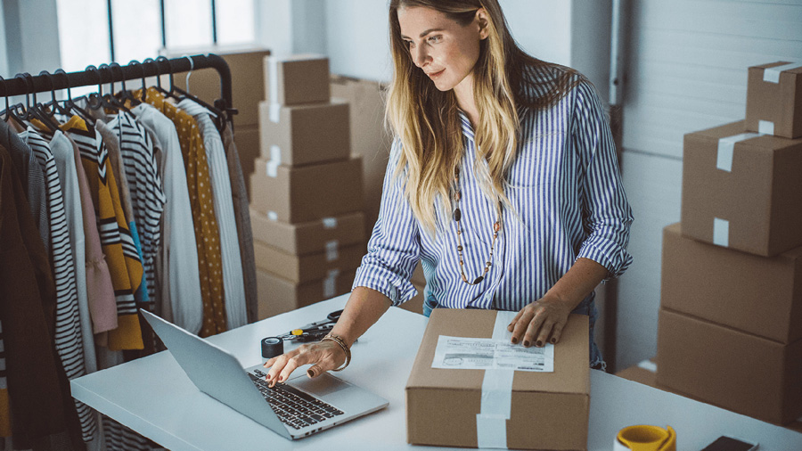 Woman looking at her laptop and preparing a box to ship.