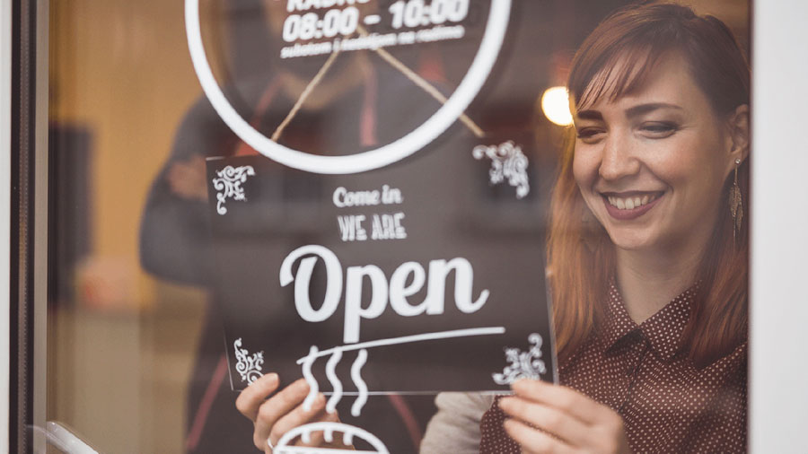 Woman smiling putting an open sign in a storefront window.